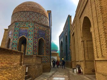 People walking in corridor of historic building against sky