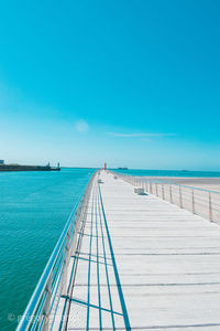 Pier over sea against clear blue sky