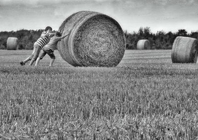 Brothers pushing hay bale on agricultural field 