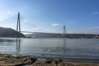 Suspension bridge over sea against cloudy sky