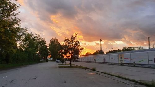 Road by trees against sky during sunset