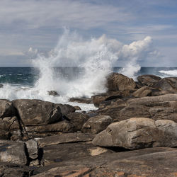 Waves splashing on rocks at shore against sky