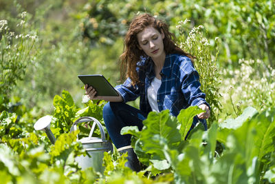 Young woman using mobile phone while sitting on plant