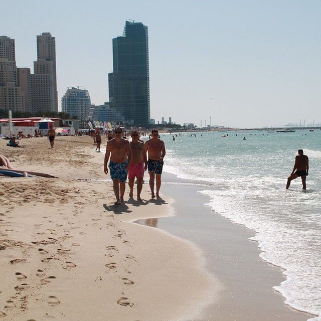 beach, sand, sea, shore, lifestyles, leisure activity, water, walking, men, person, vacations, large group of people, full length, clear sky, coastline, tourist, city life, wave, built structure