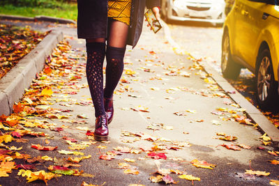 Low section of woman walking on leaves covered footpath during autumn