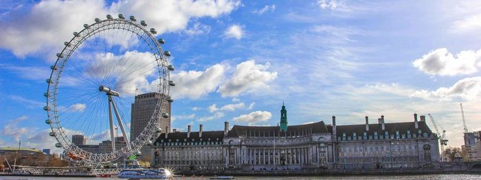 Ferris wheel in city against cloudy sky