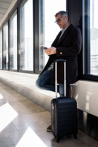 Man using mobile phone while standing by window