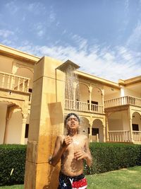 Shirtless boy taking shower against palace against sky