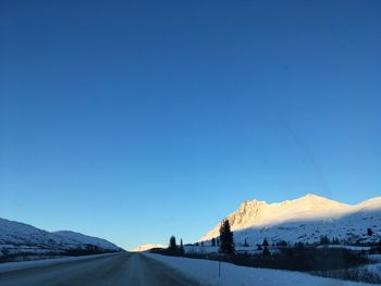 Road by snowcapped mountains against clear blue sky