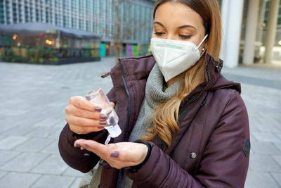 Woman with kn95 ffp2 mask using alcohol gel sanitizing her hands in city street