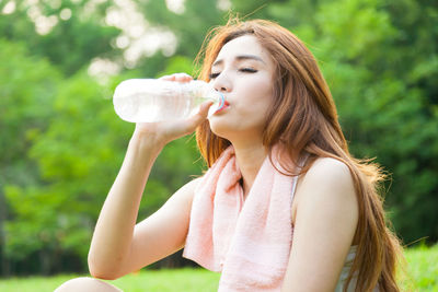 Woman drinking water from bottle against trees