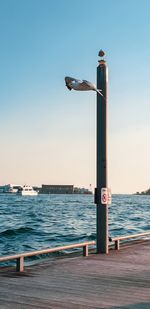 Lighthouse on pier by sea against clear sky