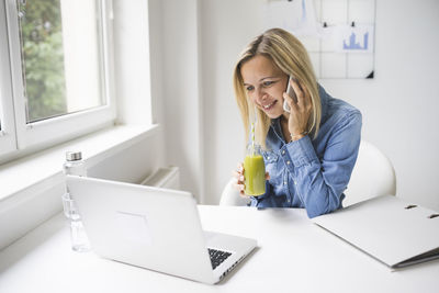 Young woman using phone while sitting on table