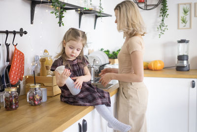Cute girl sitting on kitchen while mother working