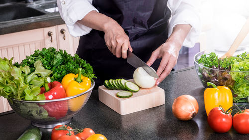 Midsection of chef cutting vegetable in kitchen