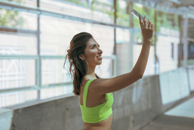 Side view of young woman holding glass while standing on footpath in city