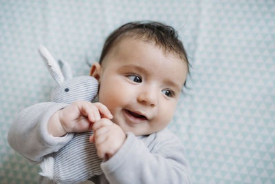 Portrait of smiling baby girl lying on bed cuddling with toy bunny