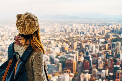 Rear view of young woman with backpack standing against cityscape