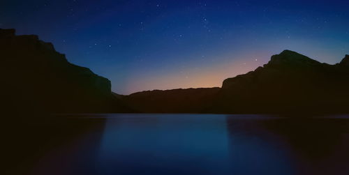 Scenic view of lake and silhouette mountains against sky at night