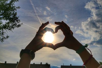 Low angle view of hand holding heart shape against sky during sunset