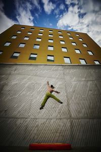 Low angle view of man climbing wall against sky