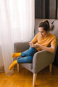 Young woman focused on her smartphone sitting in the comfortable armchair at home