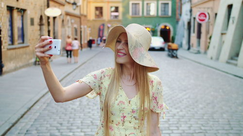 Smiling young woman taking selfie while standing on street