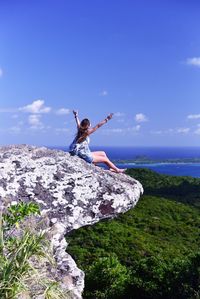 Woman standing on rock by sea against sky