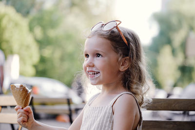 Toddler child eating cone ice cream outside near cafe. cute blonde caucasian girl licking frozen