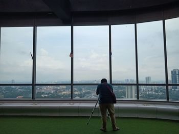 Rear view of man standing by window against sky