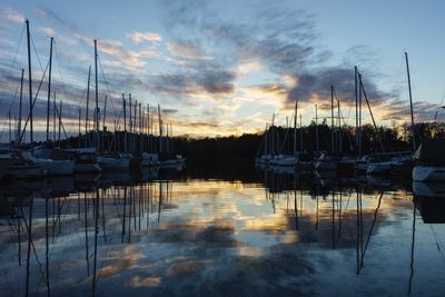 Sailboats moored in harbor at sunset
