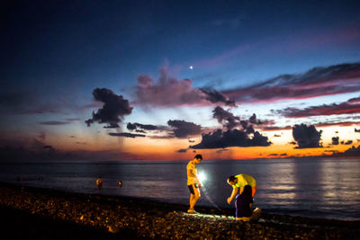 People on beach against sky during sunset