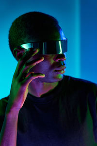 Focused cool young african american in black t shirt adjusting modern futuristic goggles while experiencing virtual reality in studio with colorful neon lights