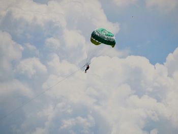 Low angle view of people paragliding against sky