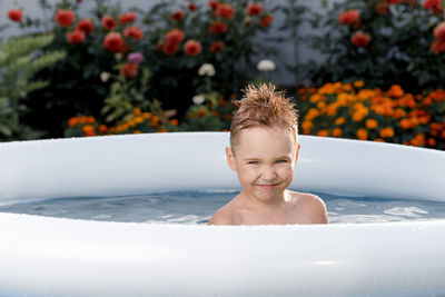 Close-up of a happy smiling five-year-old boy having fun in a blue pool outside on a sunny day. 