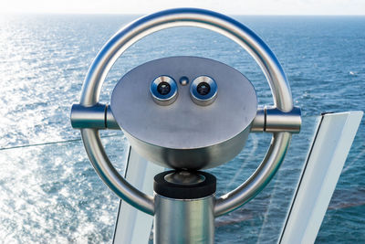 Close-up of coin-operated binoculars by sea against sky