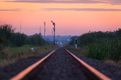 Railroad track amidst field against sky during sunset