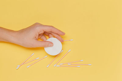 Cropped hand of person holding dental equipment against yellow background