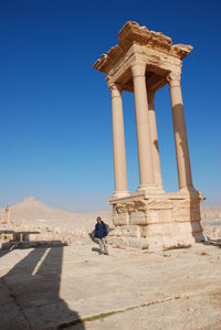 Portrait of man standing at palmyra against blue sky