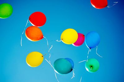 Low angle view of colorful balloons flying against clear blue sky