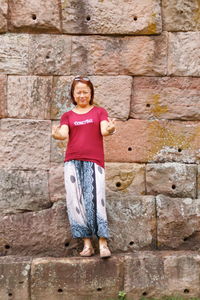 Portrait of woman gesturing against stone wall