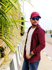 Young man wearing sunglasses while standing by plants