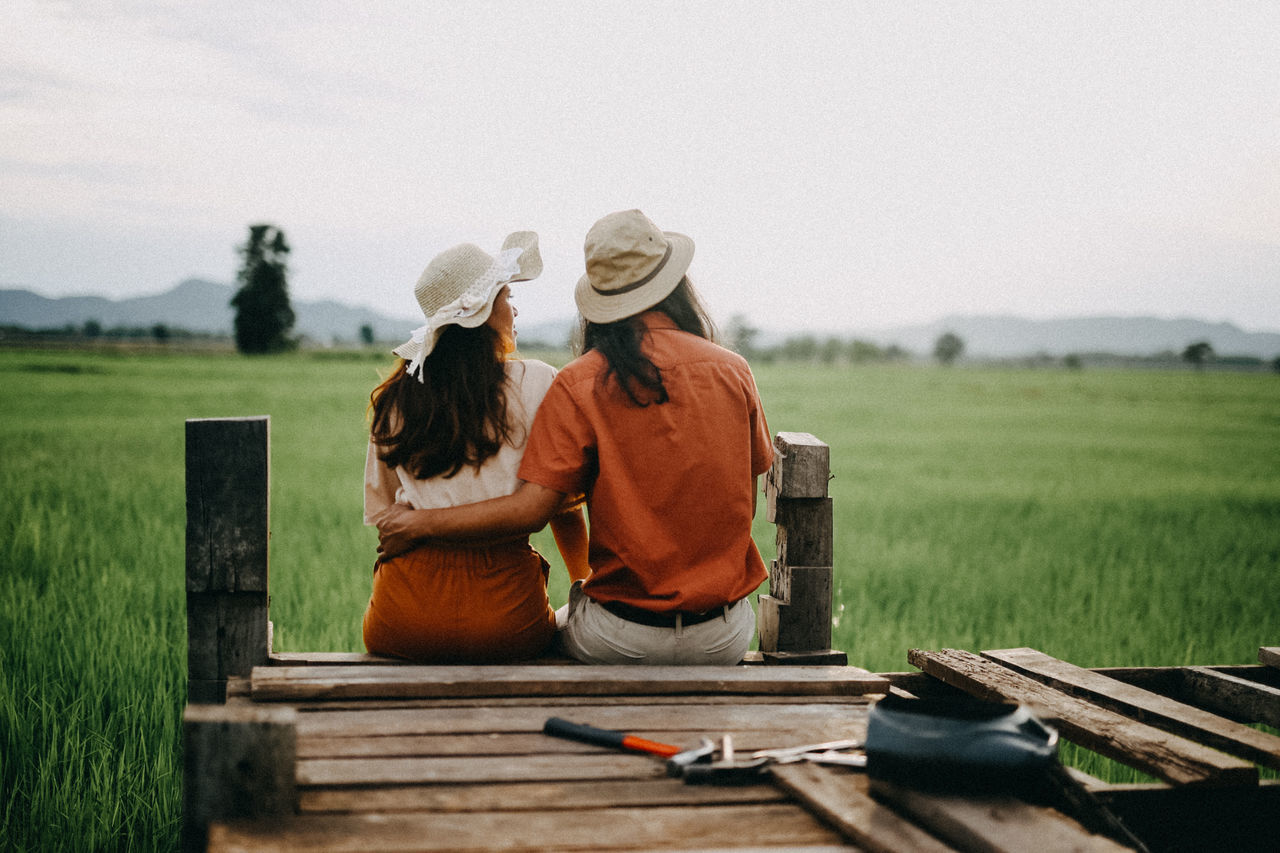 clothing, real people, women, hat, field, sky, grass, landscape, two people, nature, casual clothing, rear view, day, three quarter length, land, adult, wood - material, environment, togetherness, leisure activity, outdoors, ranch