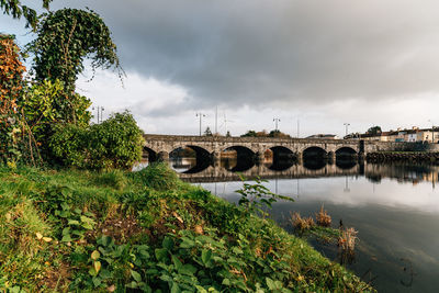 Arch bridge over river against cloudy sky