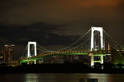 Illuminated bridge over river in city at night