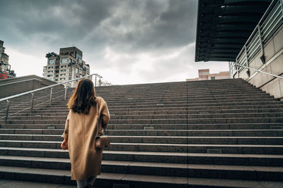 Rear view of woman standing on staircase against building