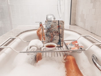 Low section of woman with drink and map bathing in bathtub