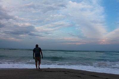 Man walking at beach against sky during sunset