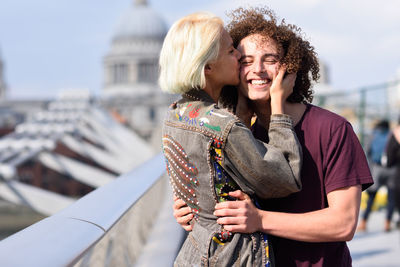 Woman kissing happy boyfriend standing on footbridge in city