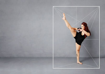 Full length of woman with arms raised against wall